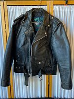 Front view of black leather motorcycle jacket with zip closure, zip pockets, snap pockets, and belted waist.