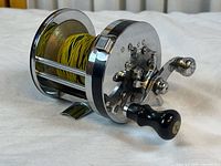 View showing side of fishing reel with handle and spool loaded with yellow braided line visible.
