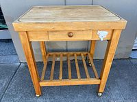 Front view of wooden butcher block kitchen cart showing drawer and lower shelf with caster wheels
