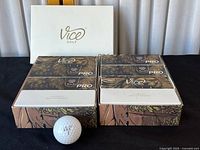 Eight Vice Golf Pro boxes, each containing three golf balls, displayed with one ball outside the boxes. Boxes feature illustrated animal (lion) design and some have missing lids.