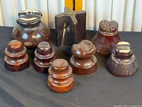 Eight brown vintage ceramic electrical insulators displayed on black surface against light curtain background.