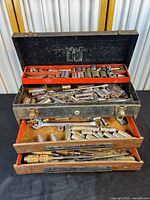 Open vintage Craftsman toolbox showing mixed hand tools inside with metal and wood components, various sockets, tools and wrenches in trays and drawers.