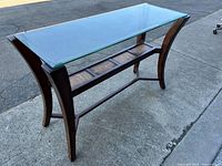 Full view of the vintage console table showing the clear beveled glass top and dark brown wooden base with curved legs and lower shelf.