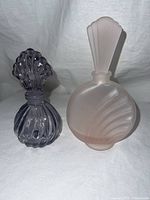 Two Bohemian glass perfume bottles, one pink frosted with fan stopper, one purple with shell stopper.