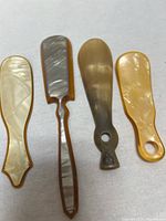 Four vintage shoe horns laid out horizontally showing the front side, made of faux tortoiseshell and lucite materials with different shapes and pearly patterns.