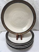 Front view of one dinner plate with graphite rim and hand-thrown spiral center, stack of remaining plates beneath.