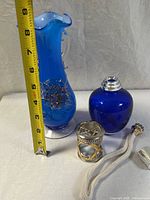 Tall cobalt blue hand-blown art glass vase measuring about 9 inches tall with applied floral details and ruffled rim next to round cobalt blue diffuser bottle and accessories.