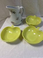 Photo of three yellow ceramic apple-shaped bowls and one white ceramic pitcher with floral and butterfly pattern