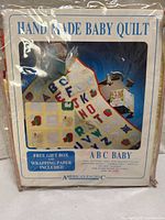 Box packaging showing image of quilt and details including "Handmade Baby Quilt", ABC Baby theme, 100% cotton, polyester filling, machine washable, size 36" x 46".