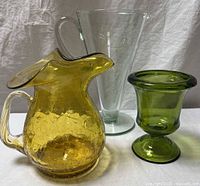 Front angle showing three vintage glass items: amber crackle pitcher, clear tall vase with handle, olive green pedestal vase.