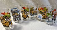 Photo shows a lineup of six vintage drinking glasses each decorated with colorful illustrations of Muppet characters from The Great Muppet Caper, including Kermit, Miss Piggy, and others
