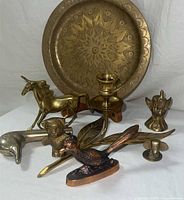 Photo showing entire lot of vintage brass decor including embossed round tray, unicorn figurine, bird sculpture, candlestick holders, wall hook, dolphin and lion figurines.