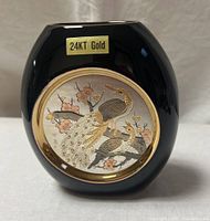 Front view of black vase with circular gold trimmed panel showing peacock and smaller bird with cherry blossoms, with 24KT gold sticker visible on front.