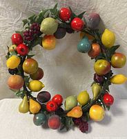 Full view of the wreath showing multiple types of faux fruits including apples, lemons, pears, grapes, and green foliage on a circular vine base.