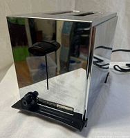 Front and side view of the chrome toaster showing the black lever and control knob with Fostoria branding plate.