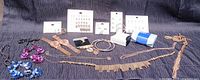 Full lot image showing assortment of jewelry and watches on dark fabric background including stones, metal bands, earrings on cards, and chains.