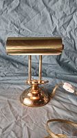Front view of polished brass piano/desk lamp with weighted base and cylindrical shade