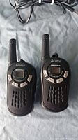 Front view of two Cobra MicroTALK walkie talkies showing LCD screens and control buttons.