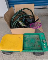 Green and yellow plastic rolling garden cart with large wheels and compartments, showing dirt and wear.