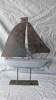 Front view of metal and wood sailboat sculpture with rectangular metal base, showing blue wooden hull and dark metal sails.