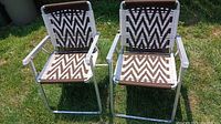 Pair of two aluminum framed patio chairs with woven brown and white chevron pattern seats and backs, shown outdoors on grass.