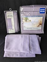 Photo showing purple Splash shower curtain in packaging and Jennifer Adams Queen size sheet set in packaging next to folded purple sheet.