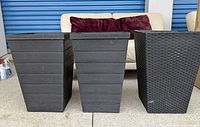 Three tall outdoor planters in dark gray/black color, showing faux wood panel texture on two planters and faux wicker/rattan texture on one planter.