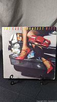 Front cover of The Cars Greatest Hits vinyl LP showing album artwork with cars and a woman's legs in red shoes on a car bumper.