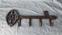 Full view of cast iron wall-mounted key-shaped key holder lying flat showing 4 hooks and decorative head design.