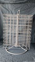 Front and side view of white metal wire rotating display rack showing square grid compartments and handle.
