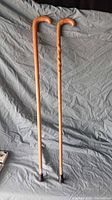 Two wooden walking canes displayed on a gray fabric background, showing full length and design differences.