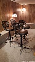 Four stools grouped showing woven rattan backs and vinyl seats in paneled room