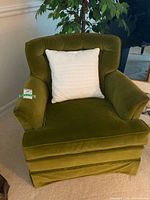 Front view of vintage green velvet Barrymore armchair with white decorative pillow seating on light carpet.