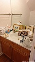 View of bathroom countertop with folded white towels, framed art pieces, bathroom toiletries, and a decorative towel holder.