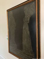 Side-angle photo of the framed brass rubbing showing two medieval figures.