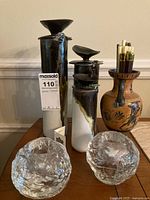 View of three Ian Phelan handmade ceramic candle holders of varying heights with bird figures on top, two clear textured glass round candle holders, and a decorative ceramic pitcher with painted designs holding pencils or matches on a wooden table.