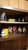 Shelf with collectible Disney, Popeye, and McDonald's glasses, black and white mugs, other kitchen items.