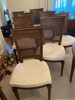 Cluster of wooden dining chairs showing cane backs and upholstered seats from front angle