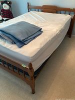 View of double wooden bed frame with mattress and folded blankets on top.