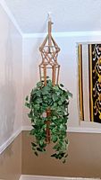 Full view of beige macramé plant hanger holding faux ivy plant, hanging from white ceiling hook.