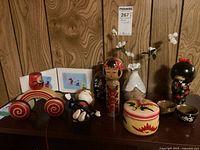 Lot of Asian-themed collectibles arranged on a wooden surface: pull toy, doll, cups, vase, kokeshi dolls, and art prints.