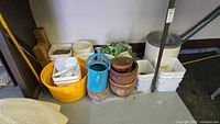Wide view showing ceramic pots, plastic containers, watering can and garden hose grouped together