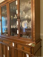 Front and side view of cherry wood two-piece china cabinet with glass doors. Shows the upper glass display cabinet and lower wood drawer and door storage sections.
