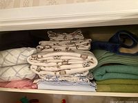 Folded sheets with owl pattern and light geometric designs visible in a closet shelf.