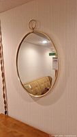 Front view of the oval mirror hanging on a wall, showing the gold metal frame and the ring at the top for hanging.