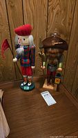 Two hand-painted wooden nutcrackers: a golfer in tartan with red beret and a night watchman with brown felt hat, spear, and lantern.