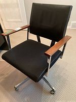 Office chair with black fabric seat, vinyl backrest, wooden armrests, and metal frame structure.