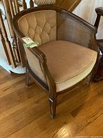 Full view of vintage barrel chair showing wood frame, tufted fabric backrest, caned sides and cushioned seat.