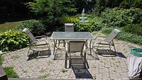 Wide angle photo capturing the entire patio set with table, four chairs arranged around it, and background greenery.