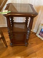 Front view of glass topped side table with caned middle shelf and wooden base shelf, showing carved legs and overall structure.